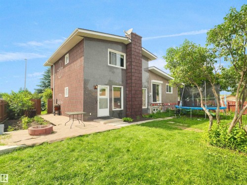 Spacious backyard featuring a large green lawn, concrete patio, and a built-in fire pit - 15603 122 Street Nw, Edmonton, AB - Outdoor With Exterior