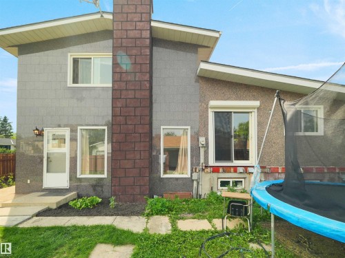Rear exterior featuring a brick chimney accent, multiple windows, a sliding glass door, and a white entry door - 15603 122 Street Nw, Edmonton, AB - Outdoor With Exterior