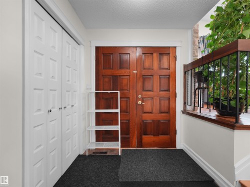 Entryway featuring rich wood-paneled double doors, white bi-fold closet doors, a detailed wood railing with black metal spindles, and light-colored walls - 15603 122 Street Nw, Edmonton, AB - Indoor Photo Showing Other Room