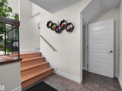Entryway featuring light neutral wall paint, wood-finish stairs with a dark wood handrail and black metal spindles, and large square floor tiles - 15603 122 Street Nw, Edmonton, AB - Indoor Photo Showing Other Room