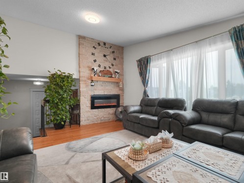 Living area featuring a stone accent wall with a built-in electric fireplace and wood-finish flooring - 15603 122 Street Nw, Edmonton, AB - Indoor Photo Showing Living Room With Fireplace