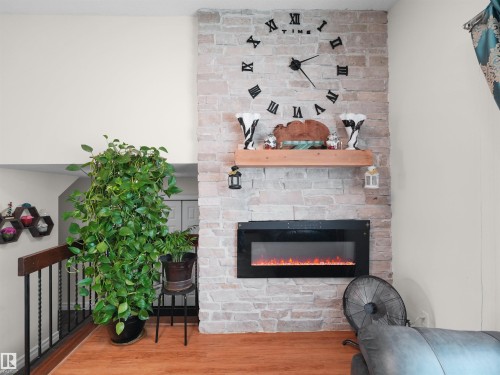 Stone-clad fireplace wall featuring a built-in electric fireplace with flame effect, a substantial wood mantel, and expansive wall space above - 15603 122 Street Nw, Edmonton, AB - Indoor With Fireplace