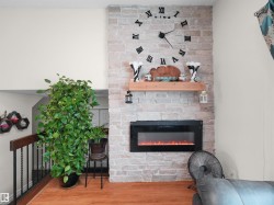 Stone-clad fireplace wall featuring a built-in electric fireplace with flame effect, a substantial wood mantel, and expansive wall space above - 