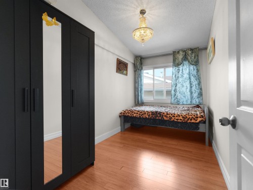 Hardwood-finish flooring featuring a window with natural light, a ceiling-mounted chandelier, and white baseboards - 15603 122 Street Nw, Edmonton, AB - Indoor Photo Showing Bedroom