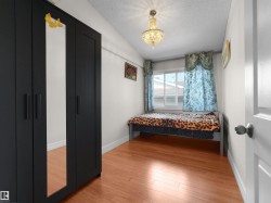 Hardwood-finish flooring featuring a window with natural light, a ceiling-mounted chandelier, and white baseboards - 