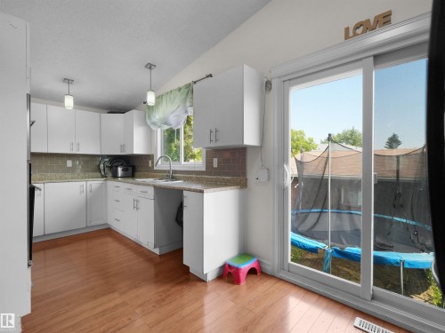 Kitchen featuring white cabinetry, wood-finish flooring, light-colored countertops, a tile backsplash, and stainless steel appliances - 15603 122 Street Nw, Edmonton, AB - Indoor Photo Showing Kitchen