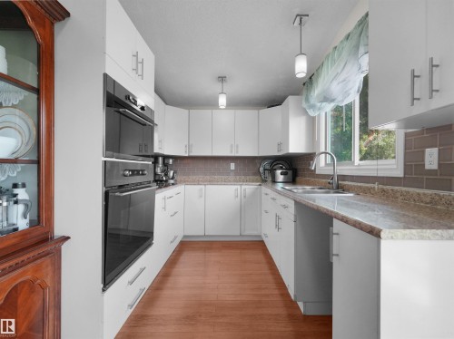 U-shaped kitchen featuring white cabinetry, wood-finish flooring, and light-toned countertops - 15603 122 Street Nw, Edmonton, AB - Indoor Photo Showing Kitchen With Double Sink