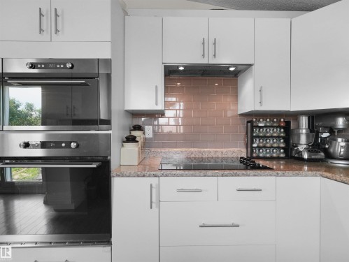 Contemporary kitchen featuring white cabinetry, stainless steel double wall ovens, a built-in cooktop, light-colored granite countertops, and a tiled subway backsplash - 15603 122 Street Nw, Edmonton, AB - Indoor Photo Showing Kitchen