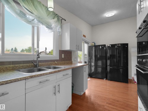 Kitchen featuring white cabinetry, a dual basin stainless steel sink, a brown tiled backsplash, and wood-finish flooring - 15603 122 Street Nw, Edmonton, AB - Indoor Photo Showing Kitchen With Double Sink