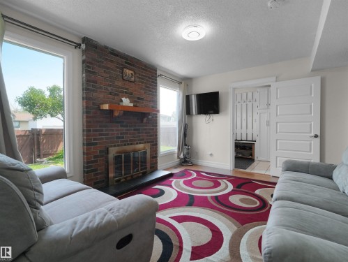 Living area featuring a brick fireplace with a wood mantle, white trim windows, and a built-in storage closet with a paneled door - 15603 122 Street Nw, Edmonton, AB - Indoor Photo Showing Living Room With Fireplace