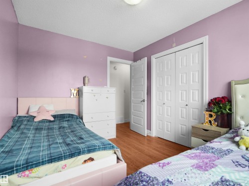 Bedroom featuring wood-finish flooring, a double-panel closet door, and a six-drawer dresser with gold-tone pulls - 15603 122 Street Nw, Edmonton, AB - Indoor Photo Showing Bedroom