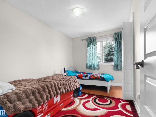 Interior room featuring a window with exterior tree views, wood-finish flooring, a white paneled door, and a ceiling-mounted light fixture - 15603 122 Street Nw, Edmonton, AB - Indoor Photo Showing Bedroom