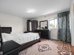 Bright bedroom featuring a single window with blinds and patterned curtains - 