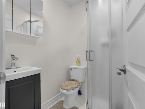 Compact bathroom featuring a white toilet, a shower with a frosted glass enclosure, a vanity with a dark wood-finish cabinet, a white rectangular sink, and a mirrored medicine cabinet - 15603 122 Street Nw, Edmonton, AB - Indoor Photo Showing Bathroom
