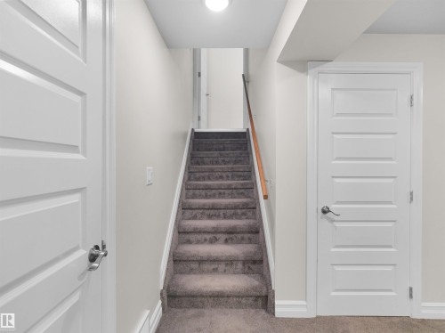 Carpeted staircase with a wood handrail, flanked by light gray walls and white trim - 15603 122 Street Nw, Edmonton, AB - Indoor Photo Showing Other Room