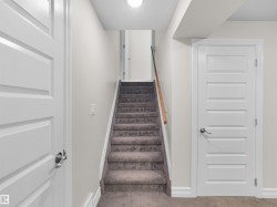 Carpeted staircase with a wood handrail, flanked by light gray walls and white trim - 