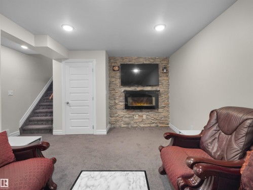 Finished lower level featuring a stone-clad media wall with an integrated electric fireplace and recessed lighting - 15603 122 Street Nw, Edmonton, AB - Indoor Photo Showing Living Room With Fireplace