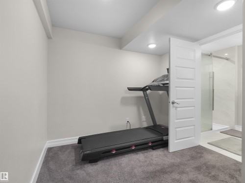 Carpeted room with recessed lighting and a five-panel interior door opening to a bathroom with a glass-enclosed shower featuring white tile - 15603 122 Street Nw, Edmonton, AB - Indoor