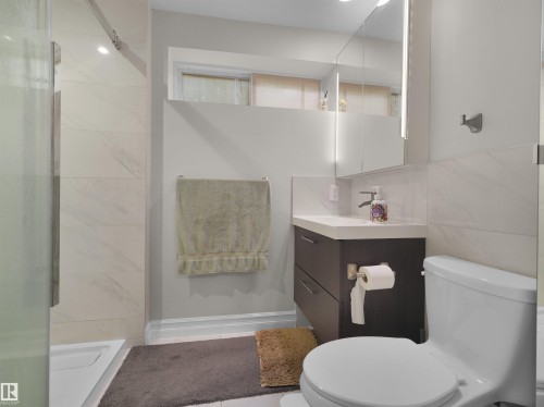 Modern bathroom featuring a glass-enclosed shower with large format tile, a dark wood-finish vanity with an integrated sink, and an illuminated medicine cabinet - 15603 122 Street Nw, Edmonton, AB - Indoor Photo Showing Bathroom