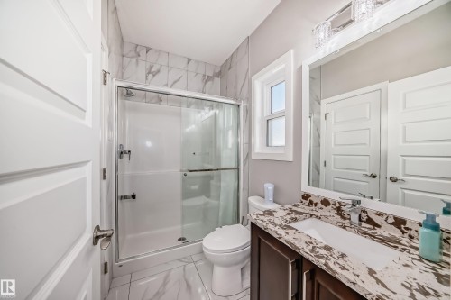 Bathroom featuring a shower with a sliding glass door, a toilet, a vanity with an integrated sink, a large mirror, and overhead lighting - 2464 15 Avenue Nw, Edmonton, AB - Indoor Photo Showing Bathroom