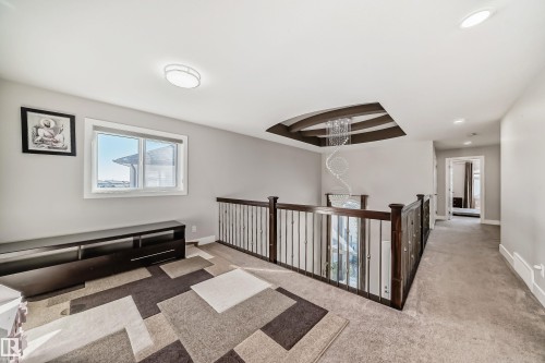 Spacious upper-level landing featuring a decorative coffered ceiling with a spiral chandelier, dark wood railing with metal balusters, and a large window providing ample natural light - 2464 15 Avenue Nw, Edmonton, AB - Indoor Photo Showing Other Room
