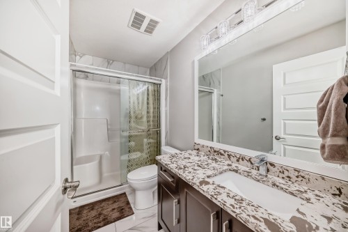 Bathroom featuring a shower with sliding glass doors, a vanity with a white rectangular sink, a speckled countertop, dark wood-finish cabinetry, and a large wall-mounted mirror - 2464 15 Avenue Nw, Edmonton, AB - Indoor Photo Showing Bathroom
