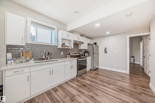 Contemporary kitchen featuring white cabinetry, a subway tile backsplash, stainless steel appliances, a window above the sink, and wood-finish flooring - 2464 15 Avenue Nw, Edmonton, AB - Indoor Photo Showing Kitchen With Double Sink