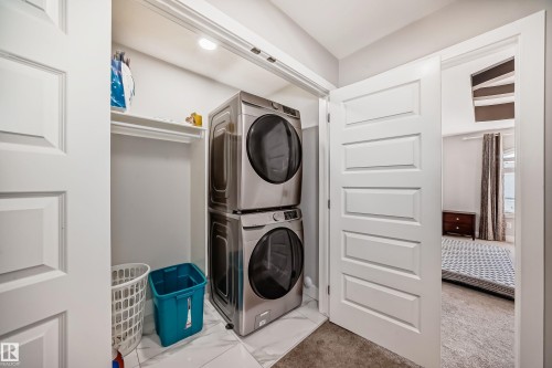 Dedicated laundry closet featuring a stacked washer and dryer, overhead shelving, and white panel doors - 2464 15 Avenue Nw, Edmonton, AB - Indoor Photo Showing Laundry Room