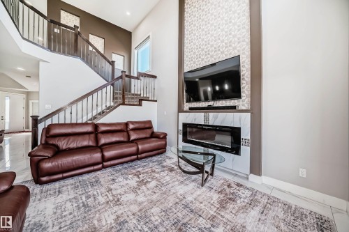 Two-story living area featuring a prominent staircase with dark wood newel posts and banisters, a large window, and light-toned walls - 2464 15 Avenue Nw, Edmonton, AB - Indoor Photo Showing Living Room With Fireplace