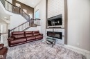 Two-story living area featuring a prominent staircase with dark wood newel posts and banisters, a large window, and light-toned walls - 2464 15 Avenue Nw, Edmonton, AB  - Indoor Photo Showing Living Room With Fireplace 