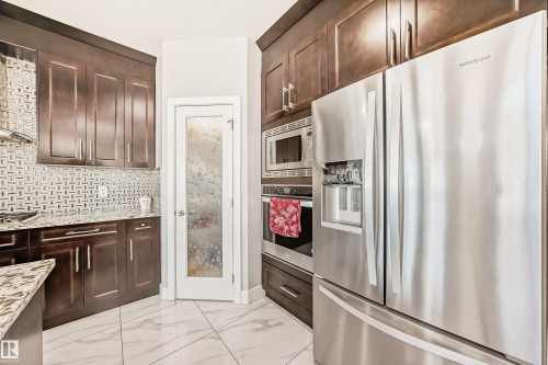 Modern kitchen featuring dark wood cabinetry, stainless steel appliances, and a mosaic tile backsplash - 2464 15 Avenue Nw, Edmonton, AB - Indoor Photo Showing Kitchen