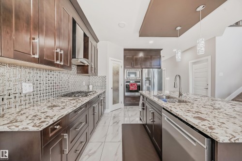 Modern kitchen featuring dark wood cabinetry, light-toned patterned countertops, and a full-height mosaic tile backsplash - 2464 15 Avenue Nw, Edmonton, AB - Indoor Photo Showing Kitchen With Double Sink With Upgraded Kitchen