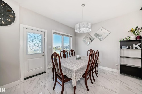 Dining area featuring large format white tile flooring, a contemporary chandelier, a built-in shelving unit, and a white paneled door with a frosted glass insert - 2464 15 Avenue Nw, Edmonton, AB - Indoor Photo Showing Dining Room