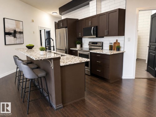 Modern kitchen featuring dark wood cabinetry, stainless steel appliances, a white subway tile backsplash, and light-toned, speckled countertops - #412 9503 101 Av Nw, Edmonton, AB - Indoor Photo Showing Kitchen