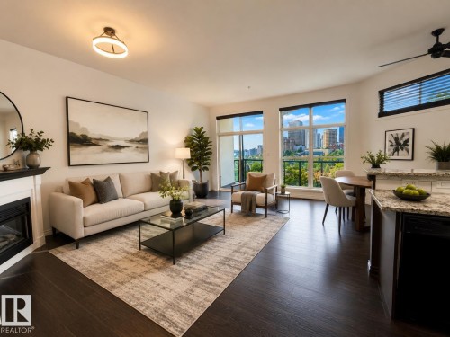 Open-concept living space featuring expansive windows, dark wood-finish flooring, a contemporary fireplace with a white mantel, and a kitchen island with a stone countertop - #412 9503 101 Av Nw, Edmonton, AB - Indoor Photo Showing Living Room With Fireplace