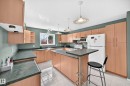 Kitchen featuring extensive light wood-finish cabinetry, dark countertops, white tile flooring, and two pendant lights - 1116 39 Street Nw, Edmonton, AB  - Indoor Photo Showing Kitchen 