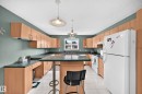 Kitchen featuring extensive light wood-finish cabinetry, dark countertops, white appliances, and tiled flooring - 1116 39 Street Nw, Edmonton, AB  - Indoor Photo Showing Kitchen With Double Sink 