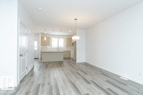 Open-concept living area featuring wood-finish flooring, a contemporary ceiling light fixture, and white walls - 6269 175A Avenue Nw, Edmonton, AB - Indoor