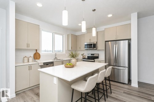 Modern kitchen featuring a central island with countertop seating, stainless steel appliances, neutral cabinetry, a subway tile backsplash, and wood-finish flooring - 6269 175A Avenue Nw, Edmonton, AB - Indoor Photo Showing Kitchen With Stainless Steel Kitchen With Upgraded Kitchen