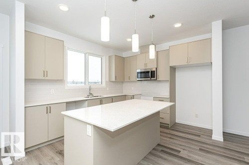 Contemporary kitchen featuring light wood-finish flooring, a central island with a light-toned countertop, and perimeter cabinetry with a matching finish - 6269 175A Avenue Nw, Edmonton, AB - Indoor Photo Showing Kitchen With Upgraded Kitchen