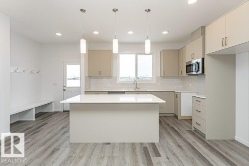 Open-concept kitchen and entryway featuring a central island with a solid surface countertop, light wood-finish flooring, recessed lighting, and pendant fixtures - 6269 175A Avenue Nw, Edmonton, AB - Indoor Photo Showing Kitchen With Upgraded Kitchen