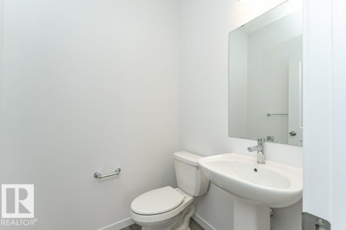 Powder room featuring a pedestal sink with chrome faucet, a rectangular wall-mounted mirror, and a matching toilet - 6269 175A Avenue Nw, Edmonton, AB - Indoor Photo Showing Bathroom