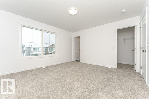 Spacious room featuring light gray carpet, white walls, a large window, a ceiling-mounted light fixture, and two interior doors - 6269 175A Avenue Nw, Edmonton, AB - Indoor Photo Showing Other Room
