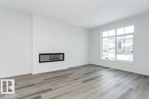 Bright living space featuring a linear electric fireplace, large picture window, and wood-finish flooring - 6269 175A Avenue Nw, Edmonton, AB - Indoor Photo Showing Living Room With Fireplace