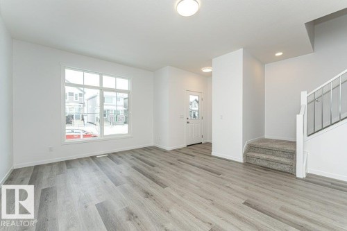 Spacious living area featuring wood-finish flooring, a large multi-pane window, and a carpeted staircase with a modern railing - 6269 175A Avenue Nw, Edmonton, AB - Indoor Photo Showing Other Room