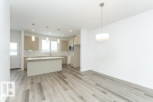 Open-concept living space featuring wood-finish flooring, a contemporary kitchen island, pendant lighting, and a drum-style ceiling fixture - 6269 175A Avenue Nw, Edmonton, AB - Indoor Photo Showing Kitchen
