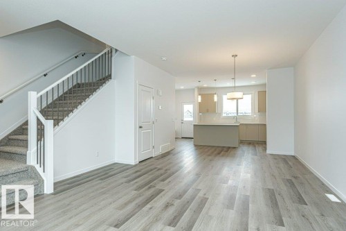 Open-concept living area featuring wood-finish flooring, a carpeted staircase with metal balusters, and a contemporary kitchen - 6269 175A Avenue Nw, Edmonton, AB - Indoor