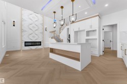 Open-concept living area featuring herringbone wood-finish flooring, a two-story accent wall with a linear electric fireplace, and a kitchen island with integrated shelving - 