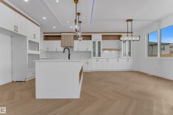 Contemporary kitchen featuring an expansive center island with an undermount sink and matte black faucet, full-height white cabinetry with gold-tone hardware, integrated appliance openings, and a white tile backsplash - 