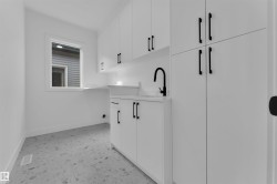 Bright utility room featuring white cabinetry, a black gooseneck faucet, a white countertop, and patterned floor tile - 